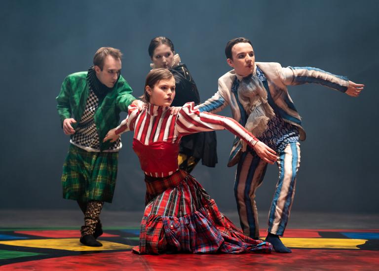 Fyra dansare i färgstarka kostymer med krås och korsetter tittar åt samma håll.