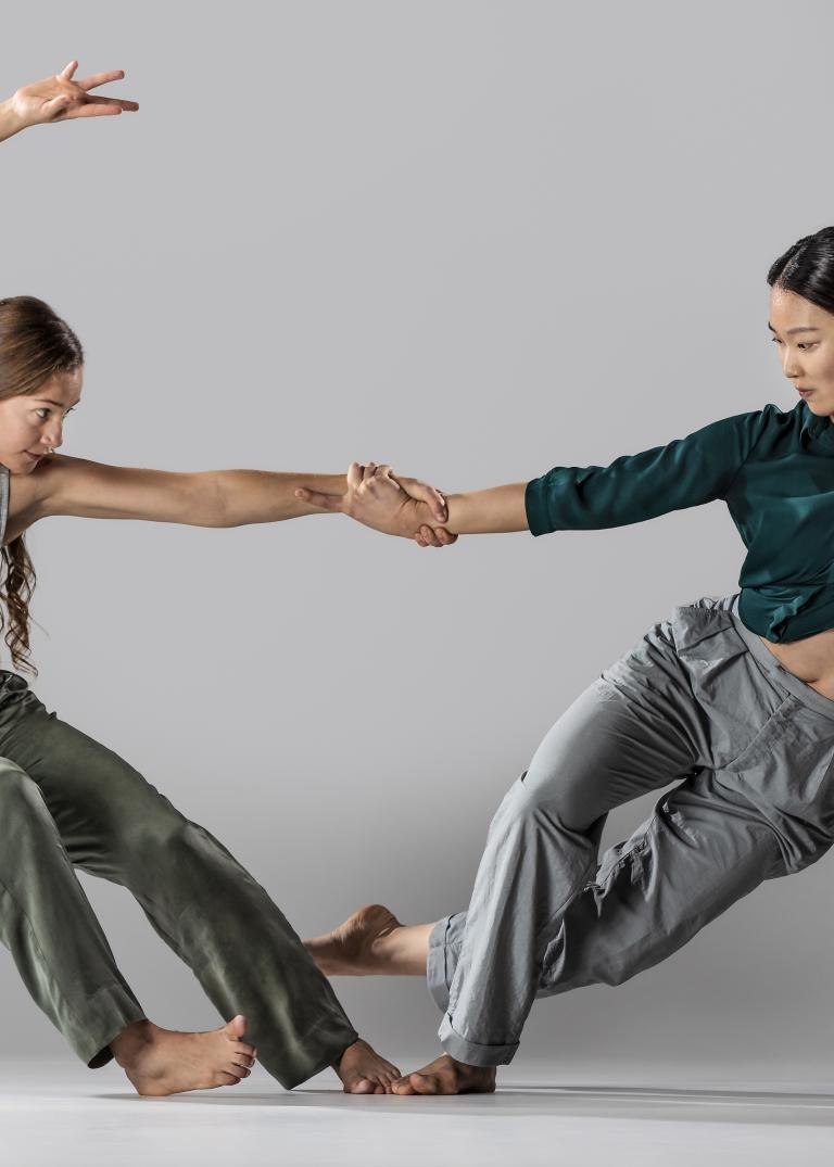 Två dansare håller varandra med en hand och balanserar på varsin fot lutandes bort från varandra.