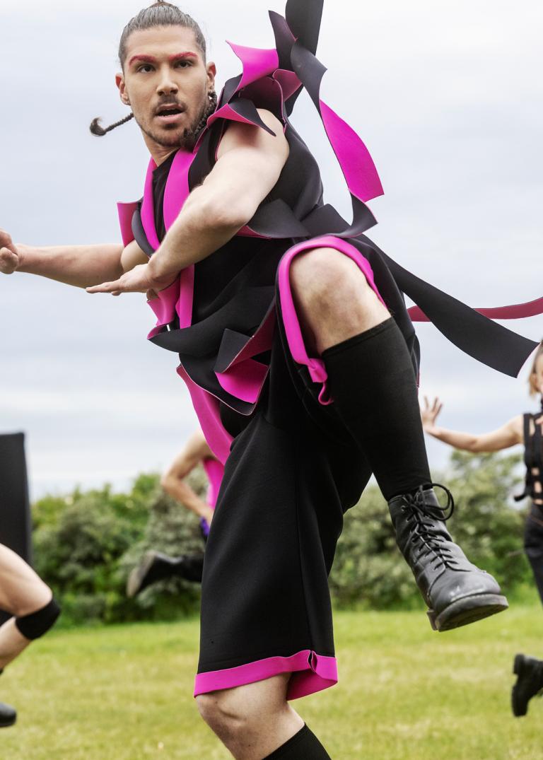 Tre dansare i kontrastrika kostymer dansar på en gräsmatta.