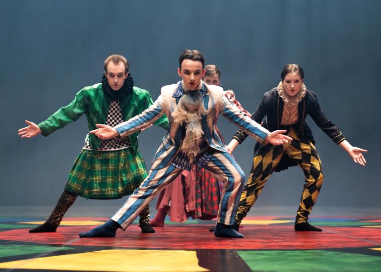 Fyra dansare i färgstarka kostymer med krusiga kragar, kiltar och volangkjolar böjer sig fram mot dig med armarna sträckta utåt och neråt.