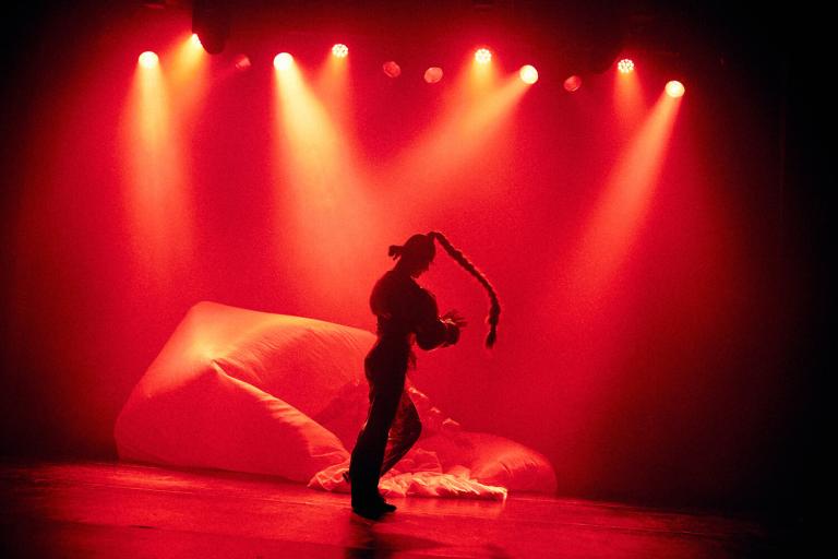En dansare står i ett hav av rött ljus i dansföreställningen SORRY NOT SORRY. 