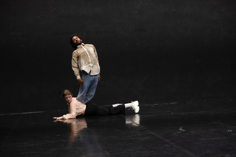 Ur dansföreställningen Megastructure, en dansare ligger på mage på golvet medan en annan dansare ser ut att snubbla över henne.