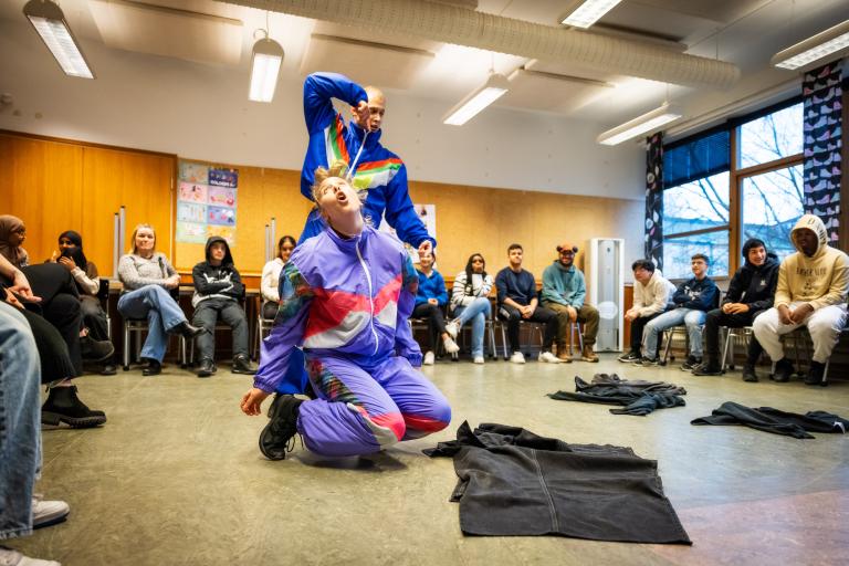 Två dansare i blå träningskläder dansar i ett klassrum i Regionteater Västs dansföreställning Sch!