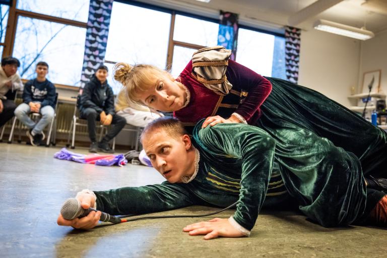 Två dansare klädda i mörkröd, mörkgrön och guldiga sammet ligger på sidan ovanpå varandra i Regionteater Västs dansföreställning Sch!