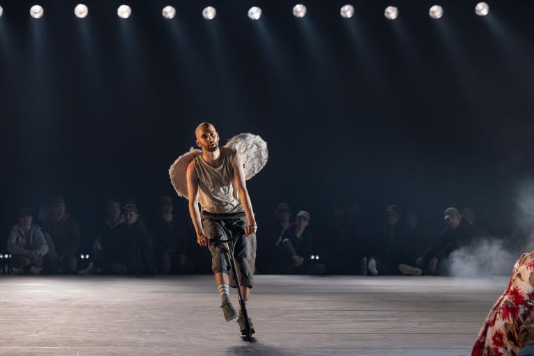 Dansaren Samuel klädd i skjorts och fluffiga änglavingar åker runt på en sparkcykel i Skånes Dansteaters jubileumsföreställning Wing Ding av koreografen Lidia Wos.