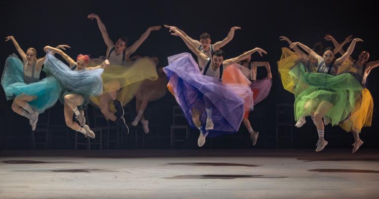 Ett tiotal dansare i tyllkjolar i alla regnbågens färger gör ett stort danshopp tillsammans med armarna lyfta som vingar i Skånes Dansteaters jubileumsföreställning Wing Ding av koreografen Lidia Wos. Foto: Tilo Stengel.