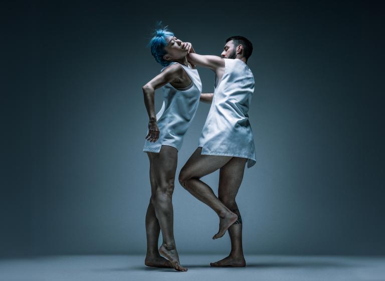 Dansarna Kat och Simone Frederick dansar mitt emot varandra med bara ben och vita, korta ärmlösa skjortor.