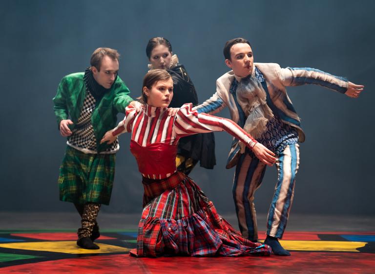 Fyra dansare i färgstarka kostymer med krås och korsetter tittar åt samma håll.