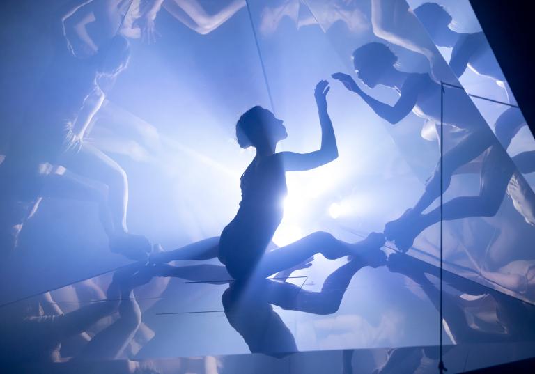 En sitter dansare i ett kalejdoskop som multiplicerar reflektioner av hennes kropp.