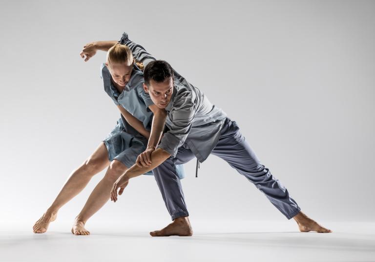 Bild på två dansare som lutar sig mot varandra i blå kläder.