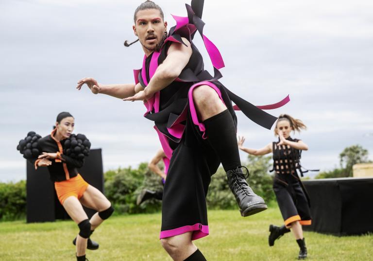 Tre dansare i kontrastrika kostymer dansar på en gräsmatta.